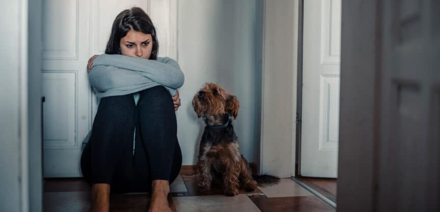 Besorgte Frau sitzt auf dem Boden und wird von einem kleinen Hund angeschaut