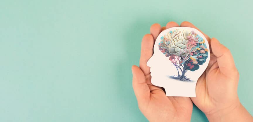 Hände halten ein ausgeschnittenes Profil mit einem kreativ gestalteten Gehirn als Baum