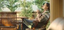 Frau in warmem Pullover genießt entspannt eine Tasse Tee auf einer sonnigen Terrasse.