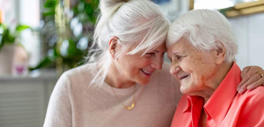 Zwei ältere Frauen lachen und genießen einen liebevollen Moment zusammen.
