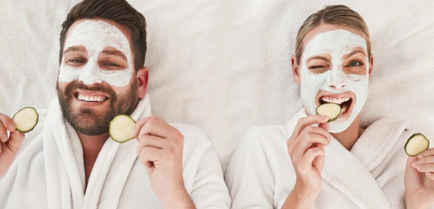 Junges Paar mit Gurkenmasken liegt lachend am Rücken.