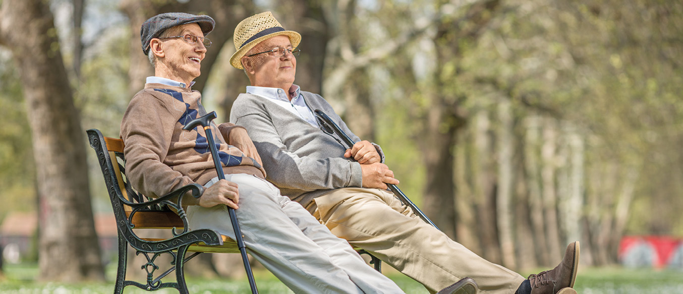Zwei alte Herren sitzen entspannt lächelnd nebeneinander auf einer Parkbank.