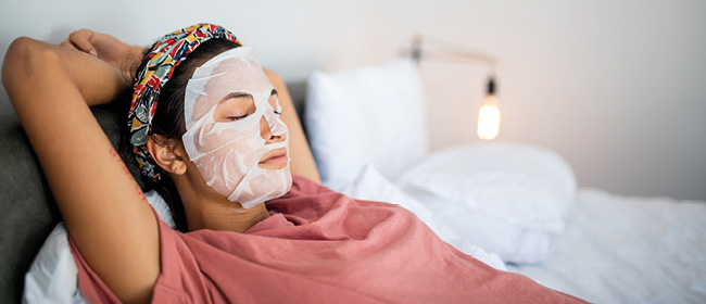 Frau mit Gesichtsmaske liegt entspannt mit geschlossenen Augen im Bett