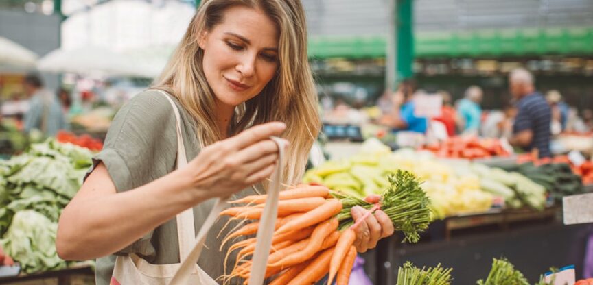 Junge Frau kauft am Markt einen großen Bund spitze Karotten mit Grün.
