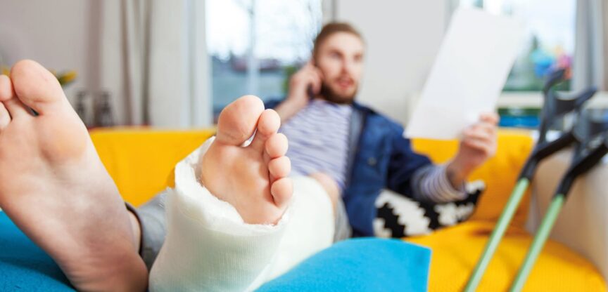 Junger Mann mit eingegipstem Unterschenkel auf Sofa.