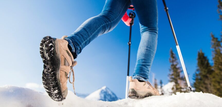 Person, von der nur die Beine zu sehen sind, wandert unter blauem Himmel über Schneefeld.