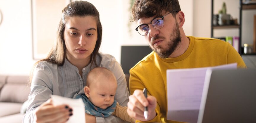 Junges Paar mit Baby füllt mit besorgtem Blick Formulare aus.