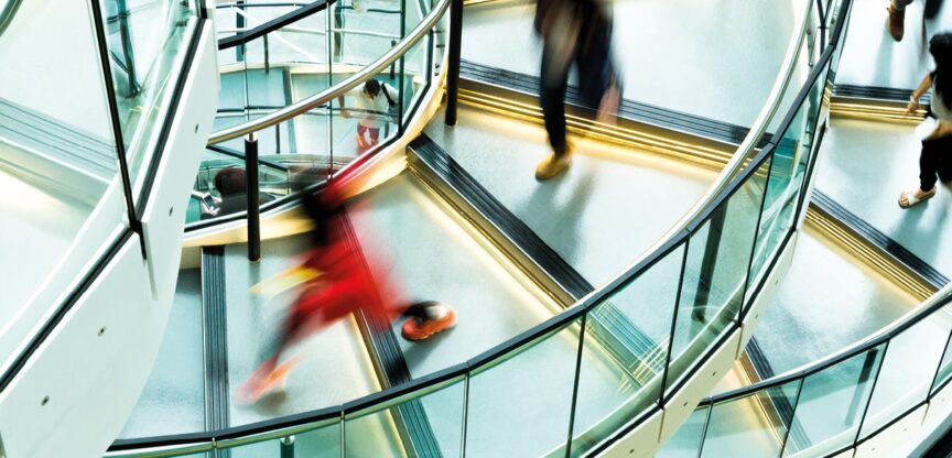 Menschen eilen über gläserne Wendeltreppe.