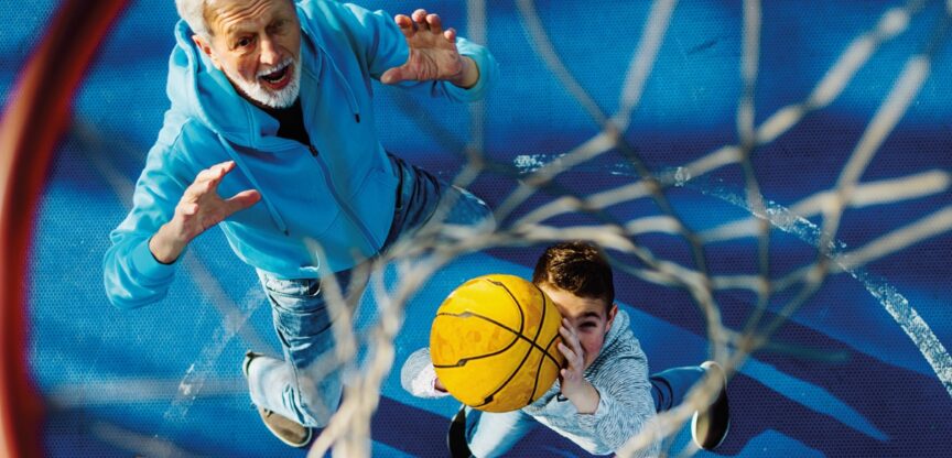 Alter Mann und Bub in blauen Trainingsanzügen beim Basketballspielen.
