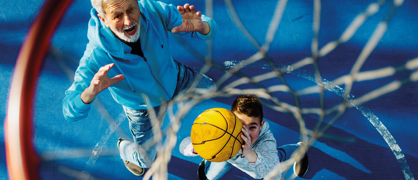 Alter Mann und Bub in blauen Trainingsanzügen beim Basketballspielen.