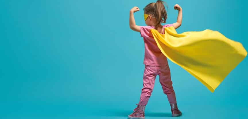 Kind in pinker Kleidung mit gelbem Umhang und Maske posiert als Superheld.