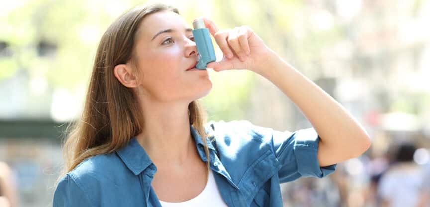 Junge Frau benutzt einen Asthma-Inhalator im Freien.