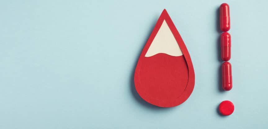 Rotes Blutstropfen-Symbol wegen Eisenmangel, neben einem Ausrufezeichen aus roten Kapseln und Tabletten auf blauem Hintergrund.