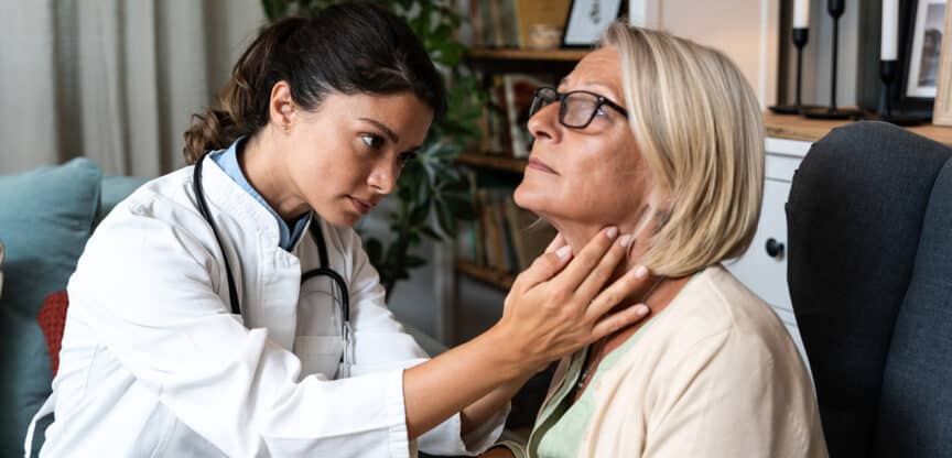 Junge Ärztin untersucht konzentriert den Hals einer älteren Patientin