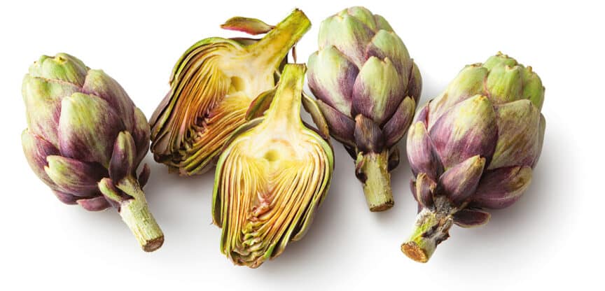Fünf frische Artischocken, davon zwei halbiert, auf weißem Hintergrund.