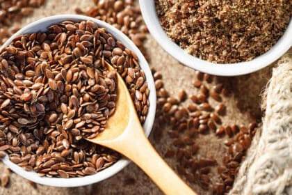 Nahaufnahme von braunen Leinsamen in einer Schale mit Holzlöffel, daneben gemahlener Leinsamen – gesunde Ballaststoffquelle und Superfood.
