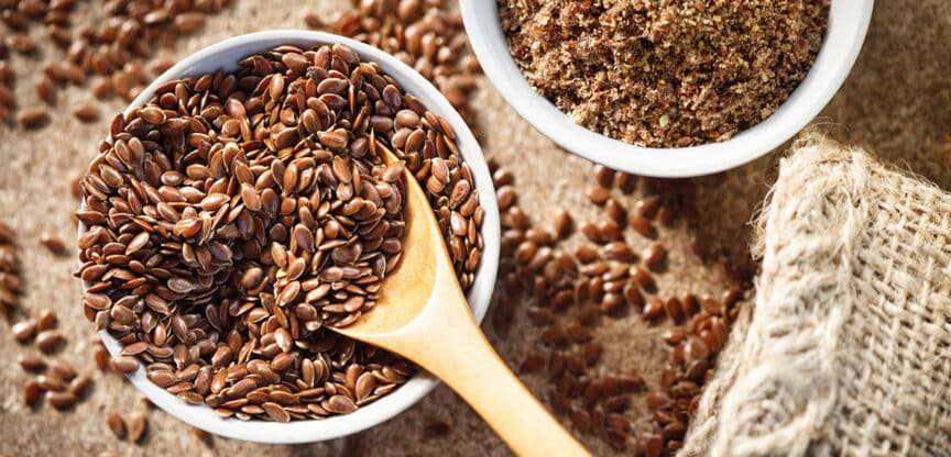 Nahaufnahme von braunen Leinsamen in einer Schale mit Holzlöffel, daneben gemahlener Leinsamen – gesunde Ballaststoffquelle und Superfood.