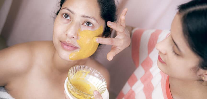 Frau bekommt gelbe, natürliche Gesichtsmaske aufgetragen