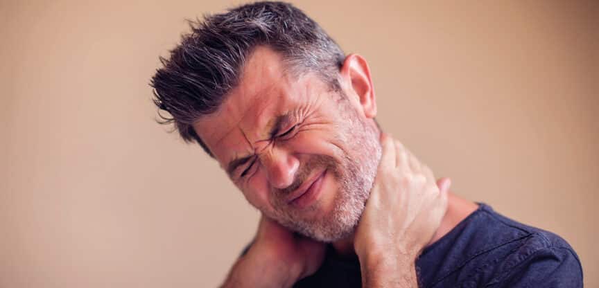 Mann greift sich vor Schmerz an den Nacken