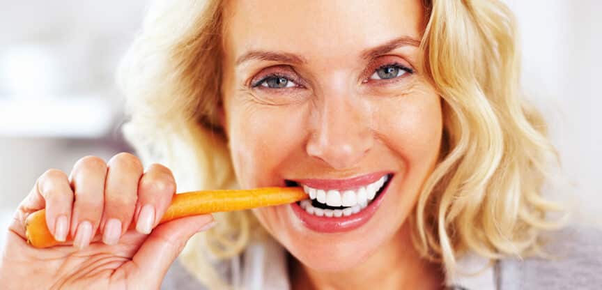 Ein Bild von einer Frau die lachend auf eine Karotte beißt.