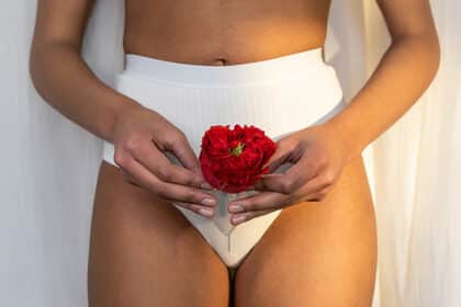 Frau in Unterwäsche hält eine rote Blume symbolisch vor ihrem Unterleib.