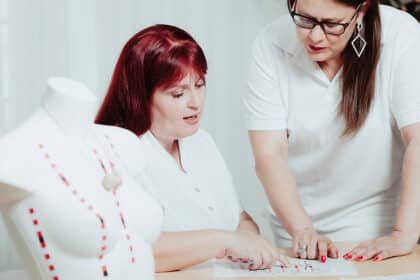 Zwei Frauen in weißer Kleidung besprechen gemeinsam ein Brustmodell und Unterlagen zur Brustkrebsfrüherkennung.