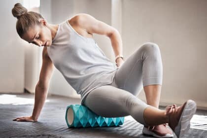 Frau sitzt auf einer Faszienrolle und massiert ihren unteren Rücken, wirkt angespannt oder schmerzgeplagt.