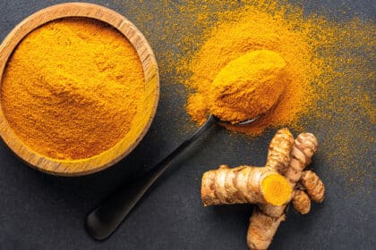 Schale und Löffel mit Kurkumapulver sowie frische Kurkumawurzeln auf dunklem Hintergrund.
