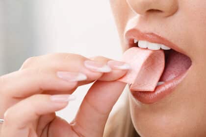 Nahaufnahme einer Frau, die ein Stück Kaugummi in den Mund legt.