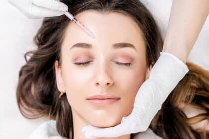 Frau liegt mit geschlossenen Augen, während eine kosmetische Injektion an der Stirn vorbereitet wird.