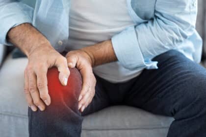 Nahaufnahme einer Person, die mit beiden Händen ein schmerzendes Knie hält.