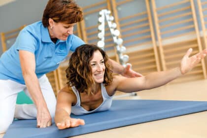 Physiotherapeutin unterstützt eine Frau bei einer Rückenübung auf einer Trainingsmatte.