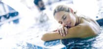 Entspannte Frau lehnt im warmen Thermal- oder Wellnessbecken am Beckenrand und genießt die wohltuende Erholung im Wasser.