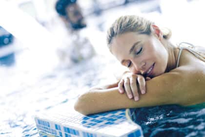 Entspannte Frau lehnt im warmen Thermal- oder Wellnessbecken am Beckenrand und genießt die wohltuende Erholung im Wasser.