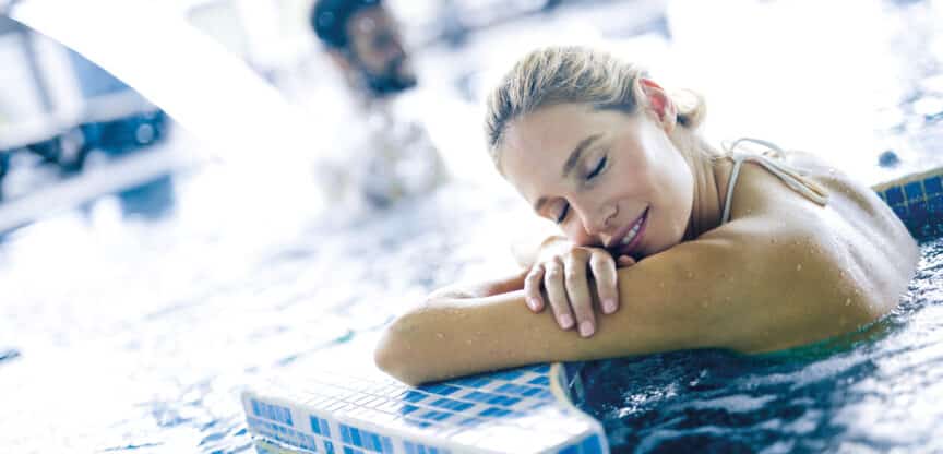 Entspannte Frau lehnt im warmen Thermal- oder Wellnessbecken am Beckenrand und genießt die wohltuende Erholung im Wasser.