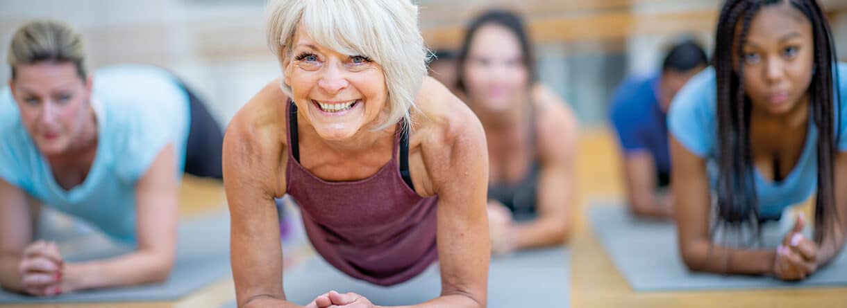 Ältere Frau trainiert mit einer Gruppe im Unterarmstütz auf Gymnastikmatten – Symbolbild für Fitness, Muskelkraft und gesundes Altern.