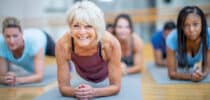 Ältere Frau trainiert mit einer Gruppe im Unterarmstütz auf Gymnastikmatten – Symbolbild für Fitness, Muskelkraft und gesundes Altern.