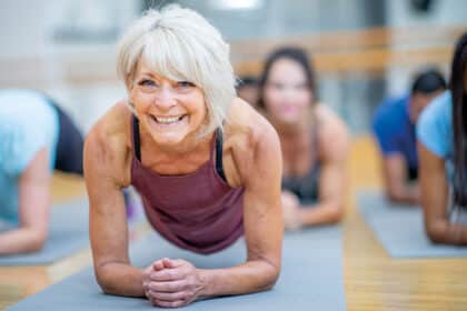 Ältere Frau trainiert mit einer Gruppe im Unterarmstütz auf Gymnastikmatten – Symbolbild für Fitness, Muskelkraft und gesundes Altern.