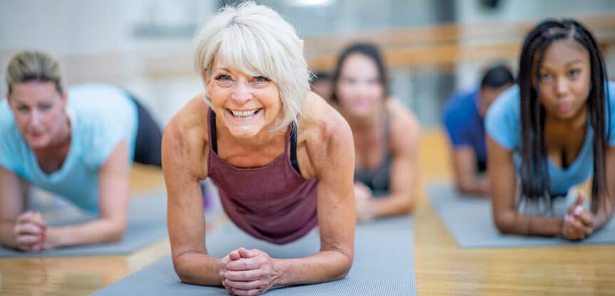 Ältere Frau trainiert mit einer Gruppe im Unterarmstütz auf Gymnastikmatten – Symbolbild für Fitness, Muskelkraft und gesundes Altern.