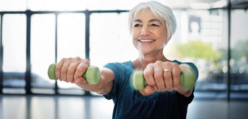Ältere Frau trainiert mit Kurzhanteln und lächelt – Symbolbild für Krafttraining, Muskelaufbau und Fitness im Alter.