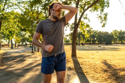 Erschöpfter Jogger wischt sich bei sommerlicher Hitze den Schweiß von der Stirn – Symbolbild für körperliche Belastung und Sport bei hohen Temperaturen.