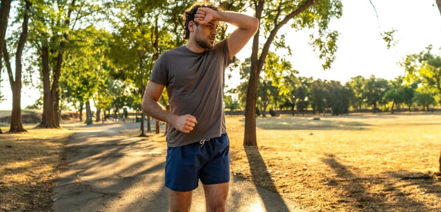 Erschöpfter Jogger wischt sich bei sommerlicher Hitze den Schweiß von der Stirn – Symbolbild für körperliche Belastung und Sport bei hohen Temperaturen.