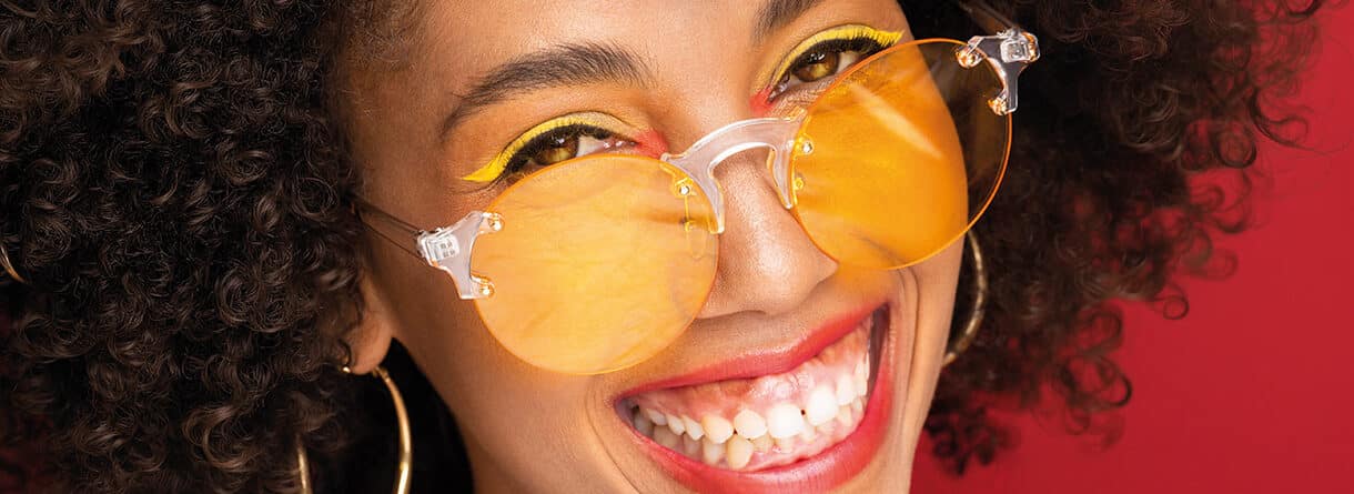 Nahaufnahme einer lächelnden Person mit gelb getönter Brille und strahlend weißen Zähnen – Symbolbild für Zahnästhetik und gesundes Lächeln.