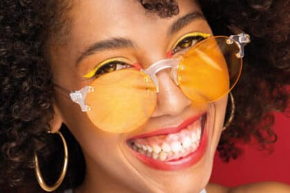 Nahaufnahme einer lächelnden Person mit gelb getönter Brille und strahlend weißen Zähnen – Symbolbild für Zahnästhetik und gesundes Lächeln.
