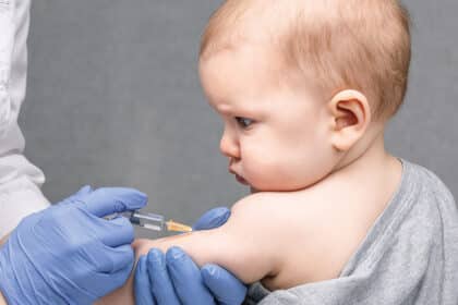Nahaufnahme eines Babys, das von medizinischem Fachpersonal mit einer Spritze in den Oberarm geimpft wird.